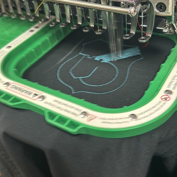 Machine de broderie multi-têtes en cours de piquage d'un motif sur vêtement noir